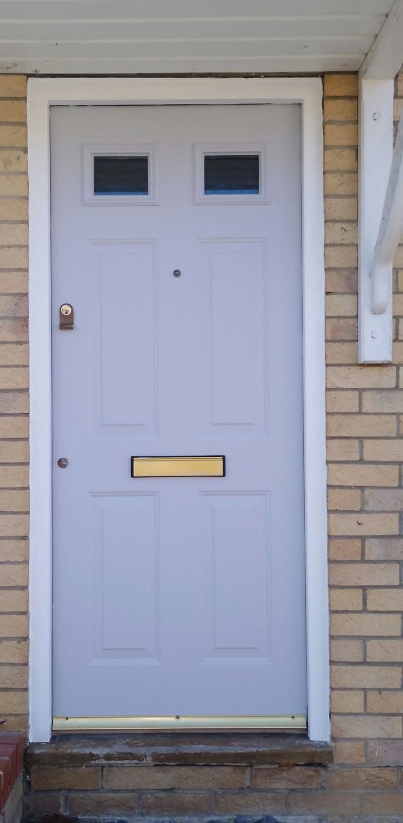 A restored front door in dove grey with a white architrave, set in yellow brick