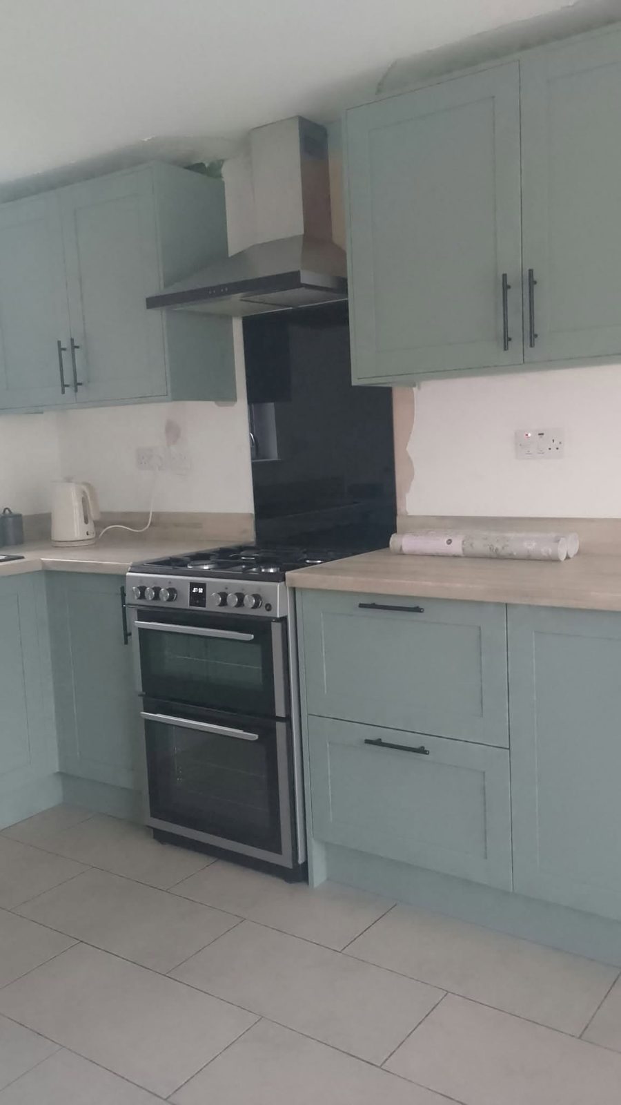 Kitchen with sage green units, a black splashback and a range cooker