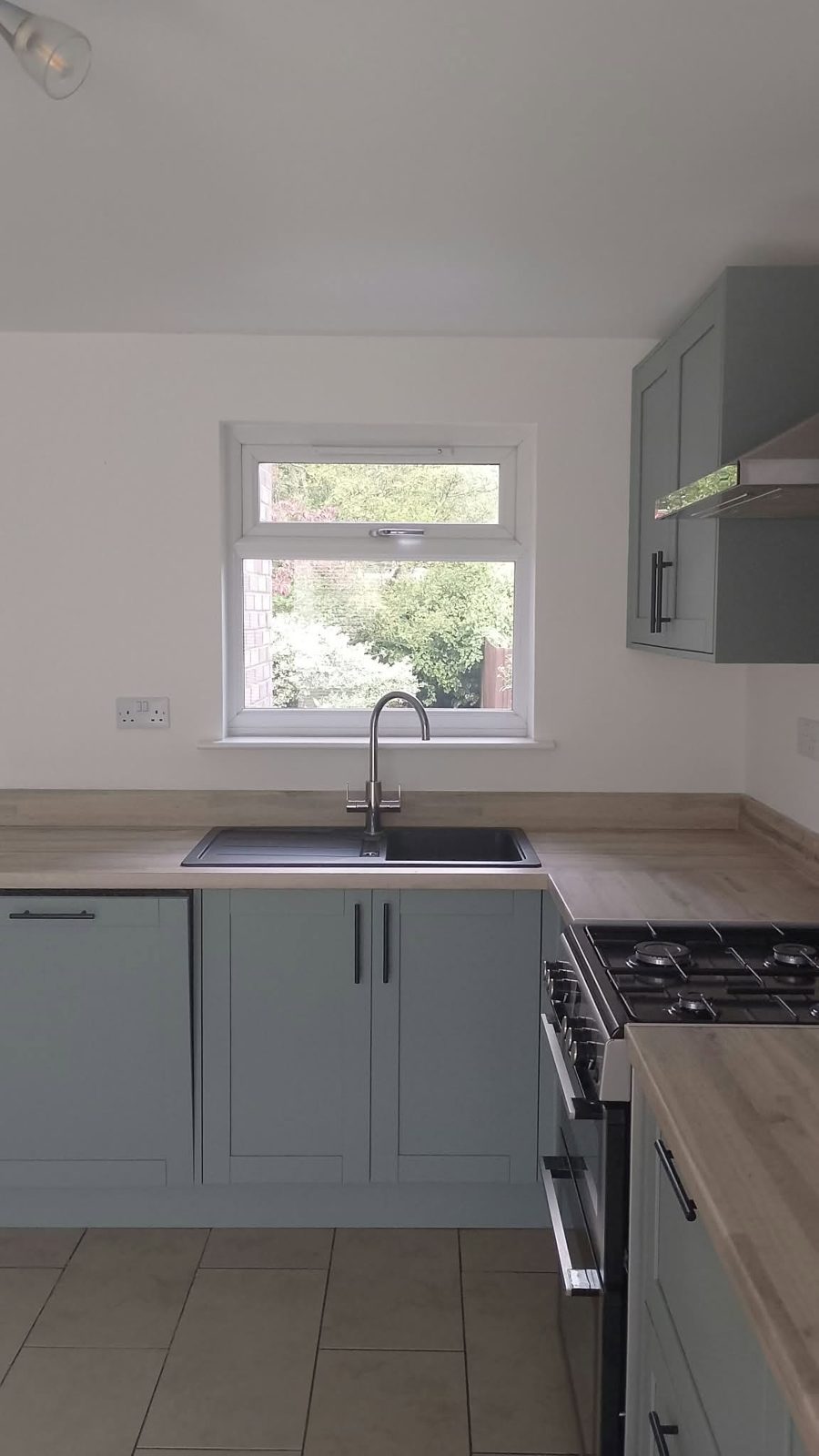 Kitchen sink under the window, with sage units and white walls