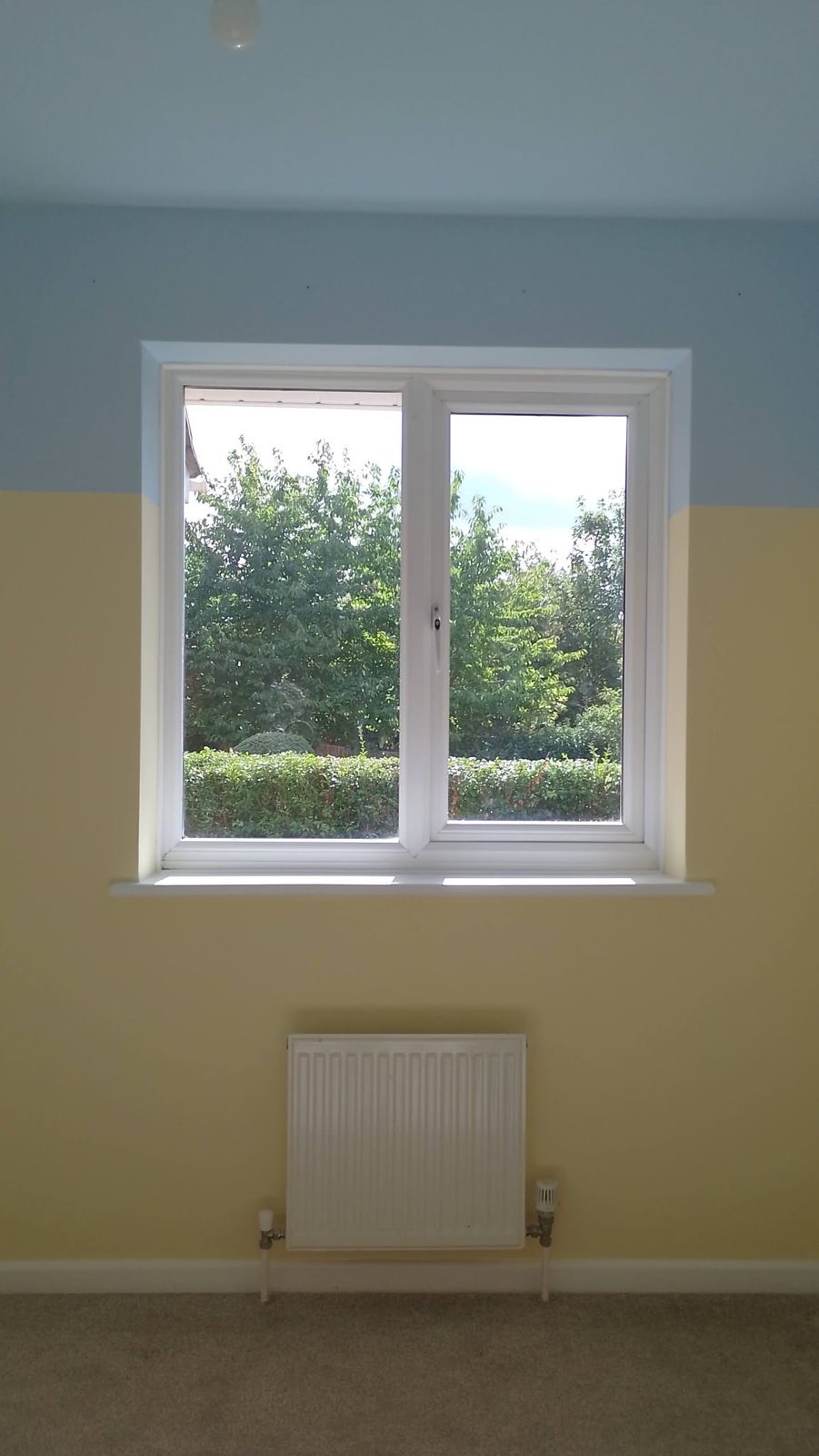A finished bedroom in pale yellow and sky blue, with a white window and radiator