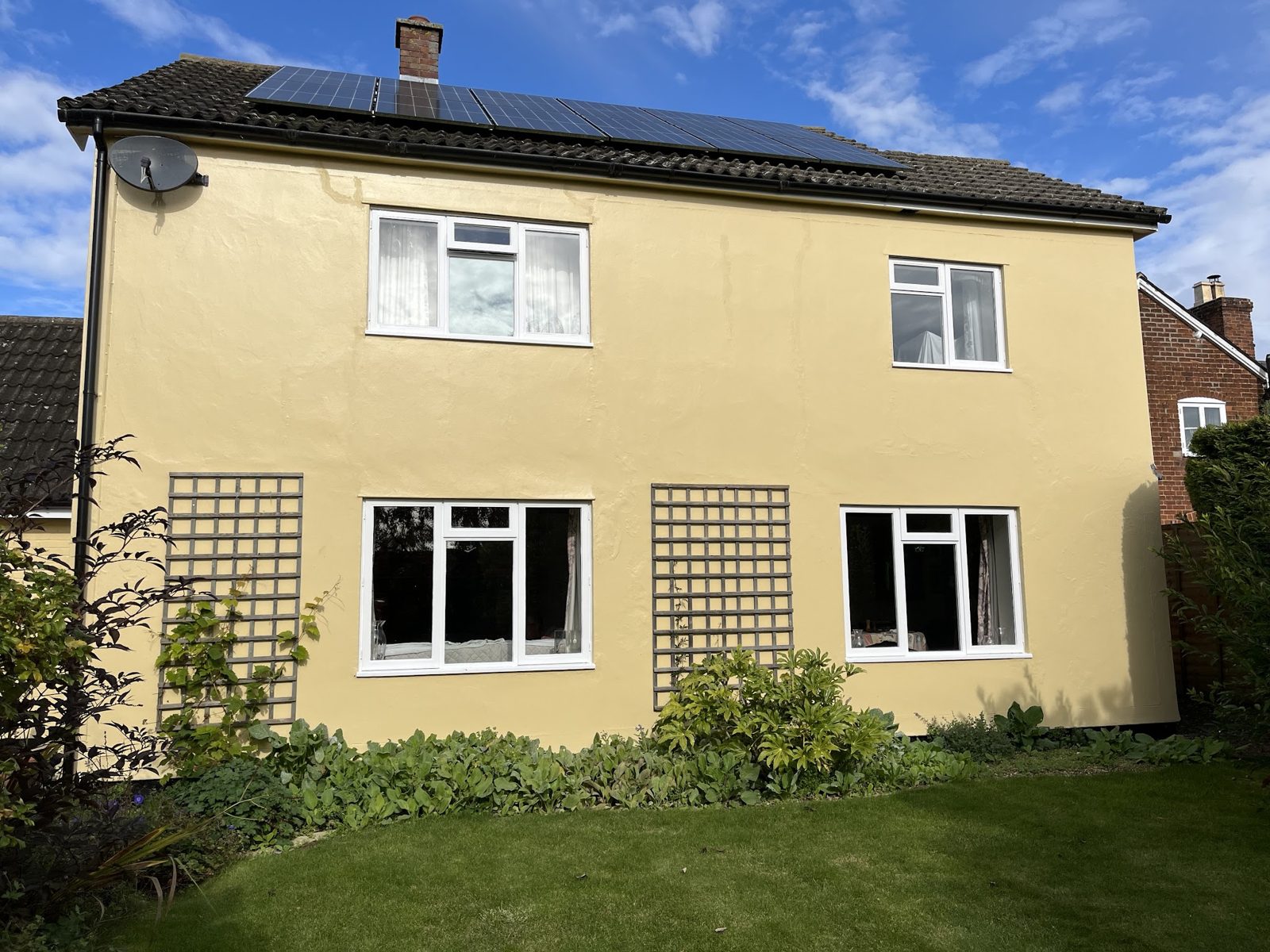 The back of a two-storey house freshly painted in pale yellow, with trellis and a lawn