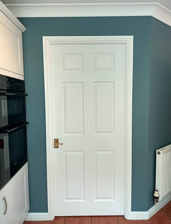 Teal wall around a white six-panel door beside the kitchen units