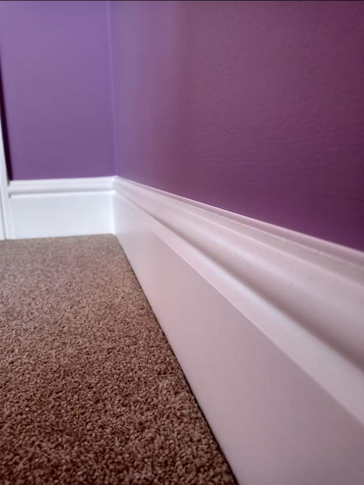 Close-up of a purple wall meeting a crisp white skirting board
