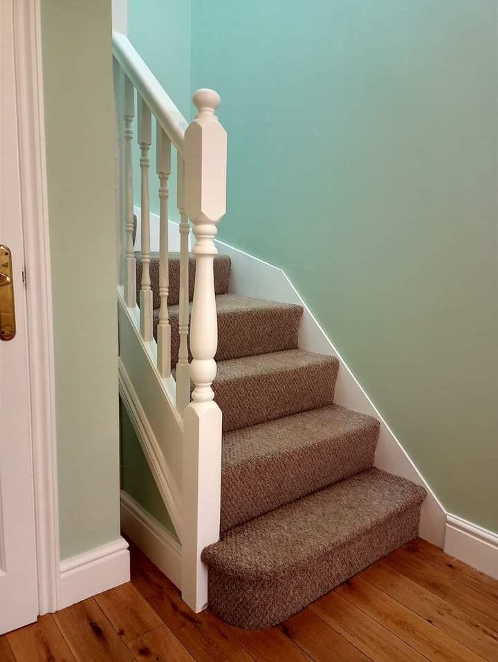 Staircase with a sage green wall and white spindles and newel post